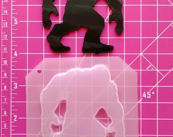 Könnte beinhalten: Eine transparente Silikonform mit der Silhouette eines Bigfoots, etwa 10 cm hoch, auf einer rosa Schneidematte mit einem Lineal.