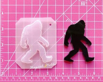 Könnte beinhalten: Eine transparente Plastikform einer Bigfoot-Silhouette. Die Form befindet sich auf einer rosa Schneidematte mit weißen Gitterlinien. Die Form ist mit "Magical Molds" beschriftet.