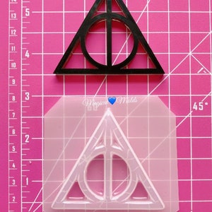 May include: Black triangular mold and a clear silicone mold, both featuring a circular shape within a triangle. The molds are on a pink grid surface. The text "Magical Molds" is visible.