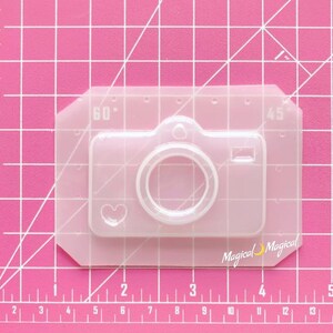 May include: Clear plastic mold for making a camera-shaped resin craft. The mold is 60 mm wide and 45 mm tall. The camera design includes a heart shape on the front.