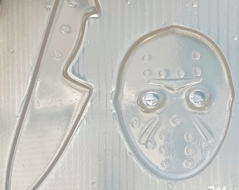 Könnte beinhalten: Eine weiße Plastikform mit zwei Formen: ein Messer und eine Hockeymaske. Die Maske hat einen weißen Hintergrund mit schwarzen Details und zwei blauen Augen.