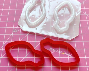 May include: Two clear plastic molds and two red silicone molds for making Christmas light ornaments. The molds are on a pink cutting mat with white grid lines.