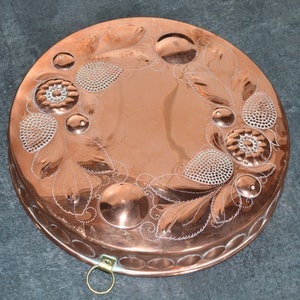May include: A round copper cake tin with an embossed design of leaves and fruit. The tin has a handle on the side.
