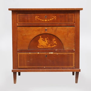 Puede incluir: Un aparador de madera con tres cajones. El cajón superior tiene una incrustación floral, el cajón del medio tiene una incrustación decorativa de un carro con dos figuras, y el cajón inferior tiene una incrustación simple. El aparador tiene un acabado de madera oscura y se apoya en cuatro patas.