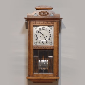 Könnte beinhalten: Eine antike Wanduhr aus Holz mit weißem Zifferblatt und schwarzen römischen Ziffern. Die Uhr hat einen dekorativen, geschnitzten Holzrahmen mit einem floralen Design.