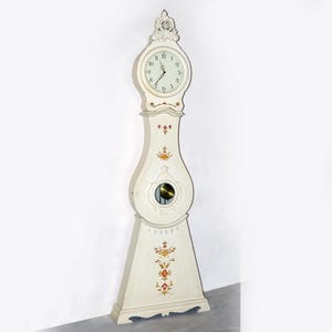 Könnte beinhalten: Eine weiße Standuhr mit einem bemalten Blumendesign und einem Zifferblatt mit römischen Ziffern.