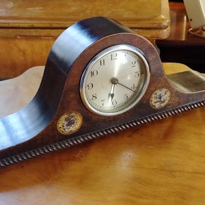 May include: A dark wood mantel clock with a silver face and black hands. The clock has a decorative design around the edge and a small, ornate design on the side.