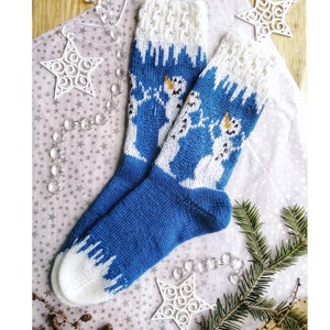 May include: A pair of knitted blue and white socks with a snowman design. The socks have a white cuff and toe, with a blue body featuring a pattern of snowmen. The socks are decorated with festive ornaments.