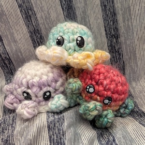 May include: Three small, round, crocheted octopus plushies with large, black, glossy safety eyes. One is light blue and yellow, one is light purple and white, and one is a vibrant mix of red, orange, and green yarn with curly tentacles.