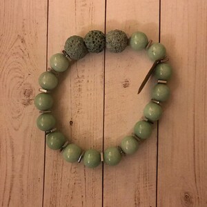 Puede incluir: Un brazalete de cuentas verdes con separadores plateados y cuentas de lava.