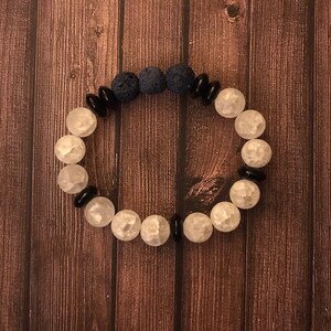 Puede incluir: Un brazalete hecho con cuentas blancas y negras, con cuentas de lava de color azul oscuro.