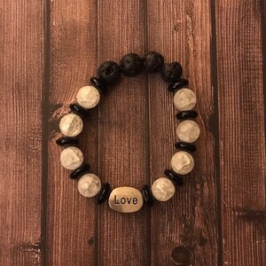 Puede incluir: Un brazalete de cuentas blancas y negras con un dije plateado que dice "Love".