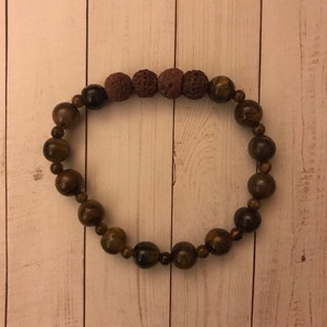 Puede incluir: Un brazalete de cuentas marrones y doradas con cuatro cuentas de lava marrón oscuro.