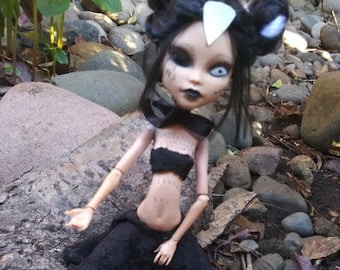 May include: A black and white doll with a white eye and black eye makeup. The doll is wearing a black top and skirt. The doll has a white horn on its head and black hair.