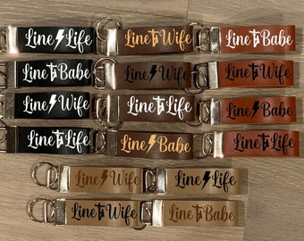 May include: A set of ten leather keychains with different phrases printed on them. The phrases include "Line Life", "Line Wife", and "Line Babe". The keychains are brown, black, and tan.