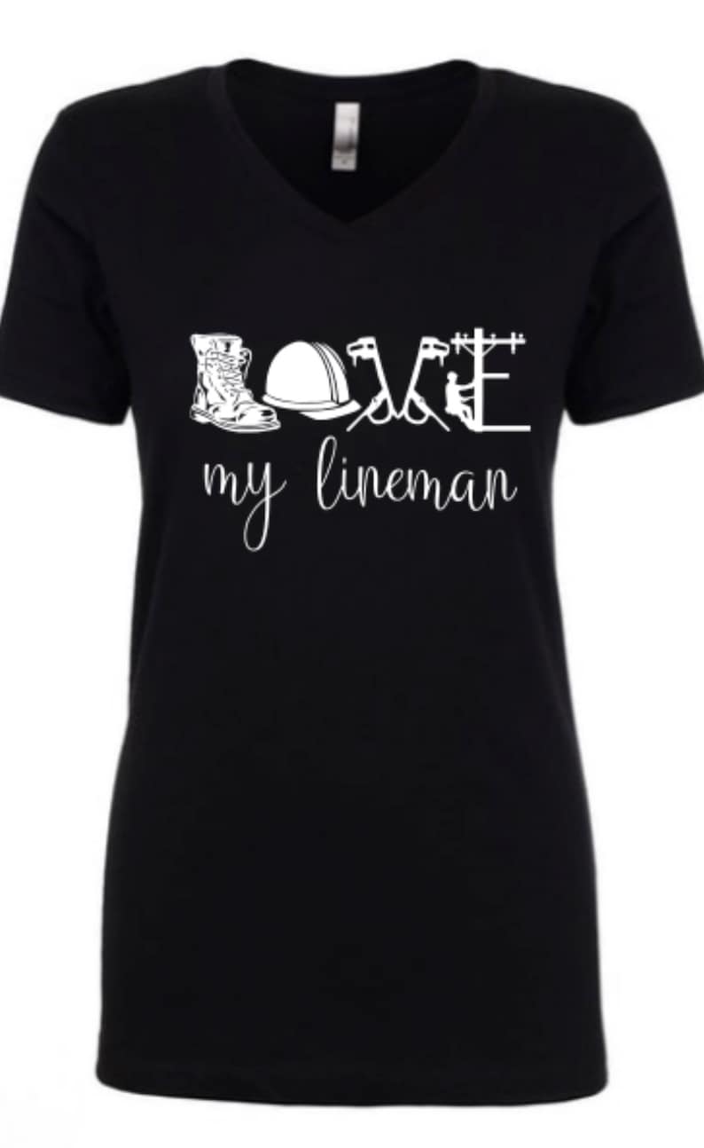 May include: Black v-neck t-shirt with a white graphic design that says "LOVE my lineman" and includes a boot, hard hat, pliers, and a lineman on a power pole.
