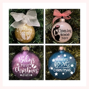 Può includere: Quattro palline di Natale con glitter e lettere bianche. La prima pallina è dorata con il testo "Expecting 2021" e due impronte bianche. La seconda pallina è bianca con il testo "Coming soon 2021" e una silhouette di una donna incinta. La terza pallina è viola con il testo "Baby's First Christmas *2020*" e un fiocco di neve e due impronte. La quarta pallina è blu con il testo "BABY'S first CHRISTMAS" e stelle bianche.