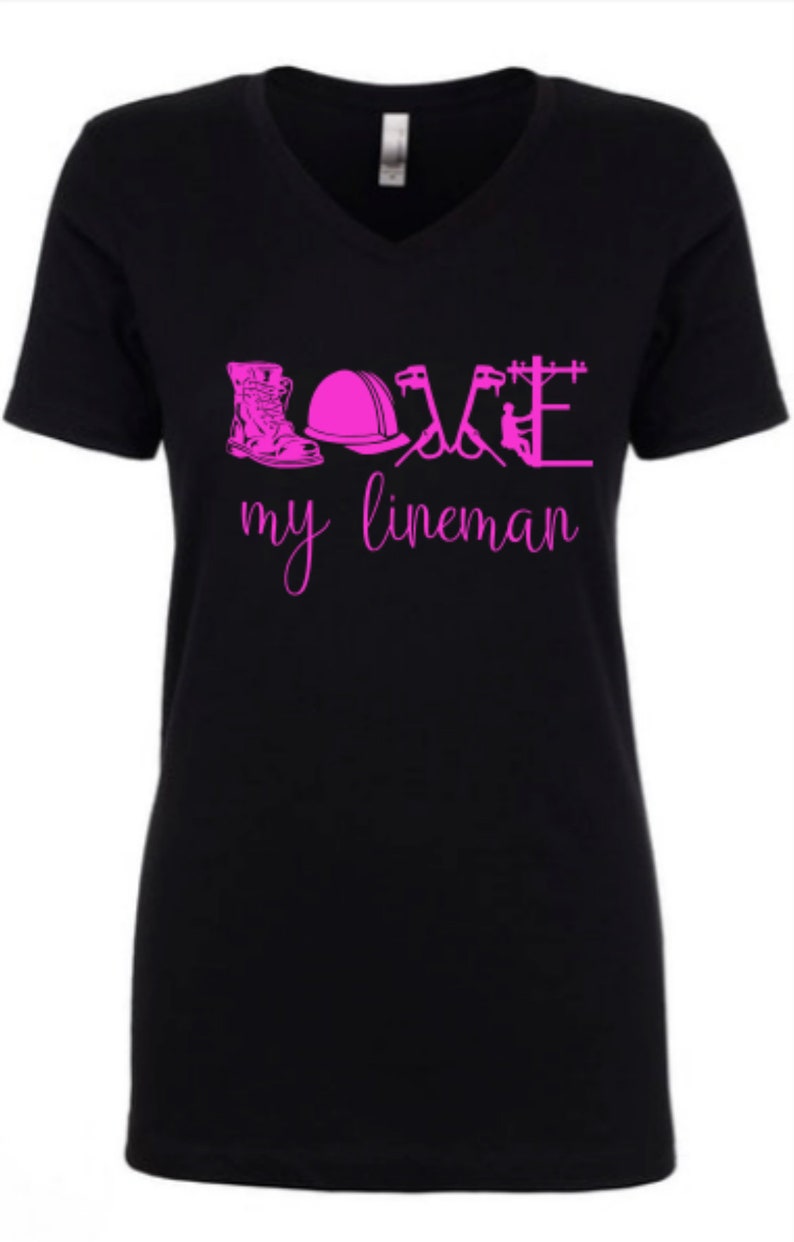 May include: Black v-neck t-shirt with pink lettering that reads "LOVE my lineman" and includes a graphic of a lineman's boots, hard hat, tools, and a power pole.