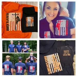 May include: A set of matching shirts and onesies featuring a distressed American flag design with a lineman silhouette and a cross. The shirts are black, navy blue, and orange. The onesies are black. The shirts have the names "Taylor", "Hoskins", and "Ray Lor" printed on them. The onesie has the text "Daddy's Little Grunt" printed on it.