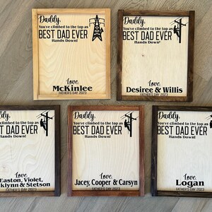 May include: Five wooden signs with a brown frame and a white background. Each sign features a silhouette of a lineman climbing a utility pole. The signs have the text "Daddy, You've climbed to the top as BEST DAD EVER Hands Down!" and a personalized message with the name and year.