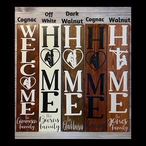 May include: Five wooden welcome signs in different stain colours. The signs feature the word "WELCOME" with a silhouette of a lineman in a heart above the "E". Each sign has a family name below the word "WELCOME". The stain colours are Cognac, Off White, Dark Walnut, Cognac, and Walnut.