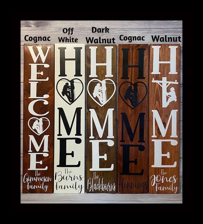 May include: Five wooden welcome signs in different stain colours. The signs feature the word "WELCOME" with a silhouette of a lineman in a heart above the "E". Each sign has a family name below the word "WELCOME". The stain colours are Cognac, Off White, Dark Walnut, Cognac, and Walnut.