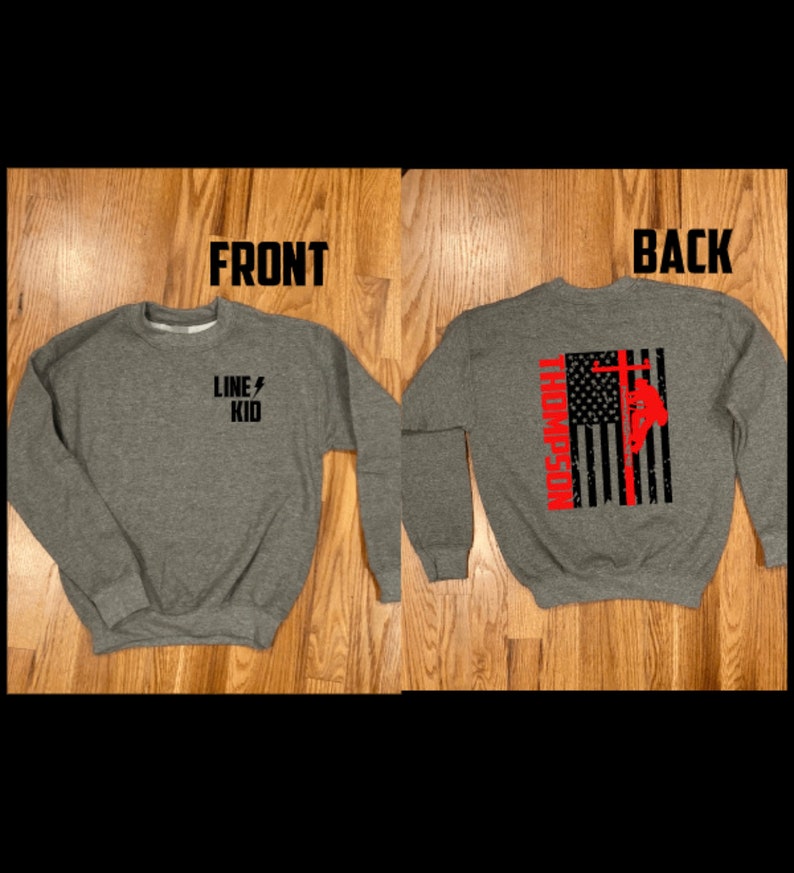 May include: A gray sweatshirt with the text "LINE KID" and a lightning bolt on the front. The back of the sweatshirt features a black and white American flag with a red silhouette of a lineman climbing a utility pole.