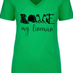 May include: Green v-neck t-shirt with a black graphic design that says "LOVE my lineman" and includes a boot, hard hat, and tools.