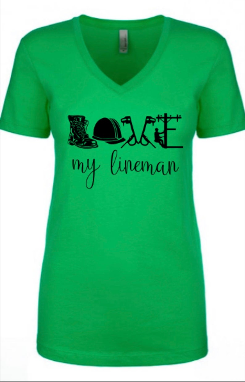 May include: Green v-neck t-shirt with a black graphic design that says "LOVE my lineman" and includes a boot, hard hat, and tools.