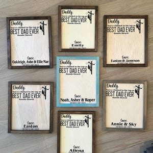 May include: Nine wooden signs with a brown frame and a light wood background. Each sign features a silhouette of a person climbing a utility pole with the text "Daddy, You've climbed to the top as BEST DAD EVER Hands Down!" and a personalized message with the name of the child or children and the year.