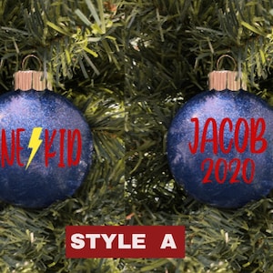 May include: Two blue Christmas ornaments with red glitter. One ornament says "Line Kid" with a yellow lightning bolt. The other ornament says "Jacob 2020".