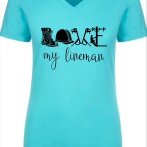 May include: A light blue t-shirt with a black graphic design that says "LOVE my lineman" with a boot, hard hat, pliers, and a lineman on a pole.