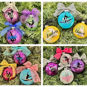 May include: A collection of 10 personalized Christmas ornaments featuring a ballerina silhouette and the year 2023. The ornaments are decorated with glitter and come in various colors, including pink, purple, blue, yellow, and white.