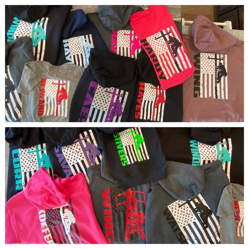 May include: A collection of hooded sweatshirts with American flag designs and various names printed on the back. The sweatshirts are in different colors, including black, grey, pink, purple, and green.
