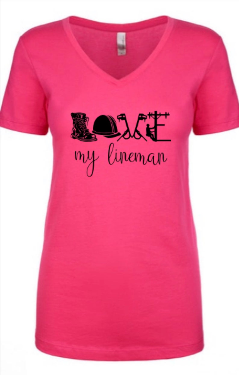 May include: Pink v-neck t-shirt with a black graphic that says "LOVE my lineman" and includes a boot, hard hat, pliers, and a utility pole.