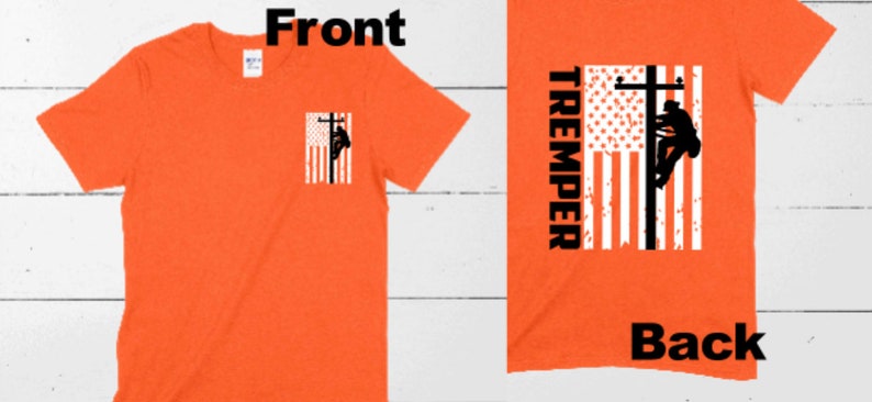 May include: Orange t-shirt with a small American flag design featuring a lineman on a utility pole on the front. The back of the shirt has a larger American flag design with the word "TREMPED" printed vertically on the left side.
