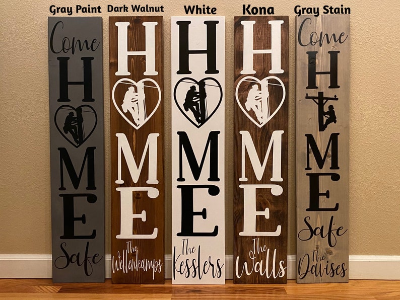 May include: Five wooden signs with the words "Come Home Safe" and a silhouette of a lineman in a heart. Each sign has a different wood stain and the last name of the family is written below the words "Come Home Safe".