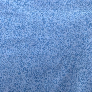 Pode incluir: Um tecido azul com um padrão floral branco. O padrão é um desenho repetitivo de pequenas flores e folhas.