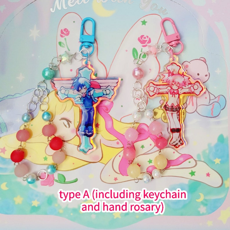 May include: Two colorful anime character cross charms with silver chains and beaded hand rosaries. The charms are attached to blue and pink keychains. The text "type A (including keychain and hand rosary)" is at the bottom of the image.