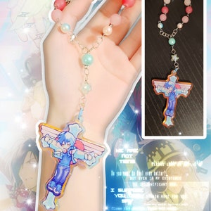 May include: A colorful beaded necklace with a charm featuring a cartoon character with blue hair and wings. The charm is shaped like a cross. The necklace is made of silver chain and has pink, white, and blue beads.