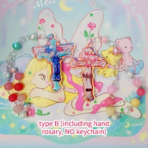 May include: A pink and blue hand-made rosary with two colorful cross charms featuring anime characters. The rosary is made with pastel pink, blue, and yellow beads. The text "type B (including hand rosary, NO keychain)" is printed on the bottom of the image.
