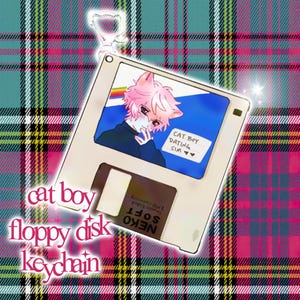 May include: A white floppy disk keychain featuring a cartoon cat boy illustration with pink hair and cat ears. The text "CAT BOY DATING SIM" is visible on the screen. The keychain also has the text "NEKO SOFT" and "2 MB Capacity".