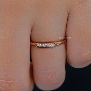 May include: A rose gold band ring featuring a small rectangular bar set with five tiny clear stones. The metal has a polished finish and the band is thin. The text "CUTE CARATS" is engraved in small letters on the side of the rectangular bar.