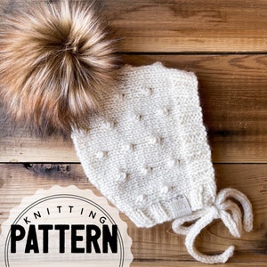 Puede incluir: Un gorro de bebé de punto blanco con un pompón de piel marrón y blanco. El gorro tiene un patrón texturizado y se ata en la parte inferior. El gorro está etiquetado con "LOOPS". La imagen incluye el texto "KNITTING PATTERN".