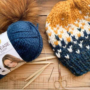 Puede incluir: Un gorro de punto azul y blanco con un patr&oacute;n amarillo y blanco. El gorro est&aacute; hecho con hilo Lion Brand Cool Ease Thick & Quick. El hilo tambi&eacute;n se muestra en la imagen, junto con agujas de tejer y tijeras.
