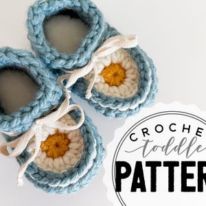 May include: Handmade blue crochet toddler booties with a daisy design. The booties feature a white and yellow centre, white trim, and cream-coloured laces. The word "LOOPS" is on a brown leather tag. The image also includes a graphic that says "CROCHET toddler PATTERN".