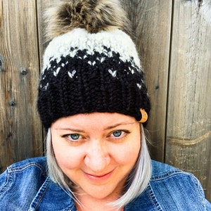 Puede incluir: Un gorro de punto negro y blanco con un pomp&oacute;n blanco. El gorro tiene una etiqueta de cuero negro en el lateral.