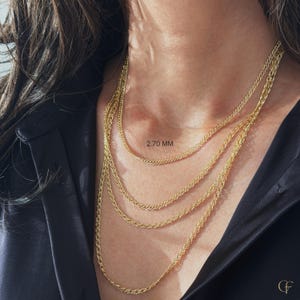 May include: A layered gold chain necklace featuring four strands of varying lengths. The chains have a textured, woven link design. The text 2.70 MM is visible near the top chain, indicating the width of the chain links in millimeters.