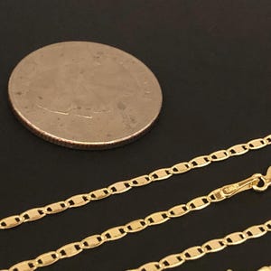 May include: A gold chain necklace with a mariner link style. The chain is lying on a black surface next to a US quarter.