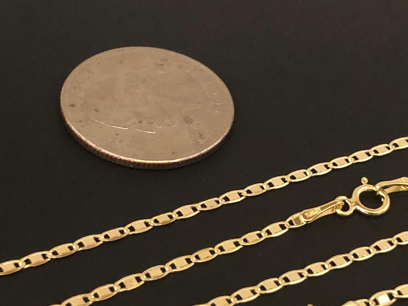 May include: A gold chain necklace with a mariner link style. The chain is lying on a black surface next to a US quarter.